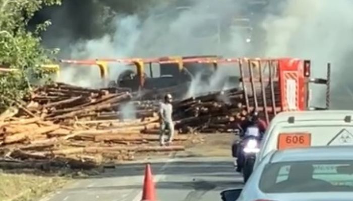 Carreta carregada com madeira tomba, pega fogo e interdita BR-101